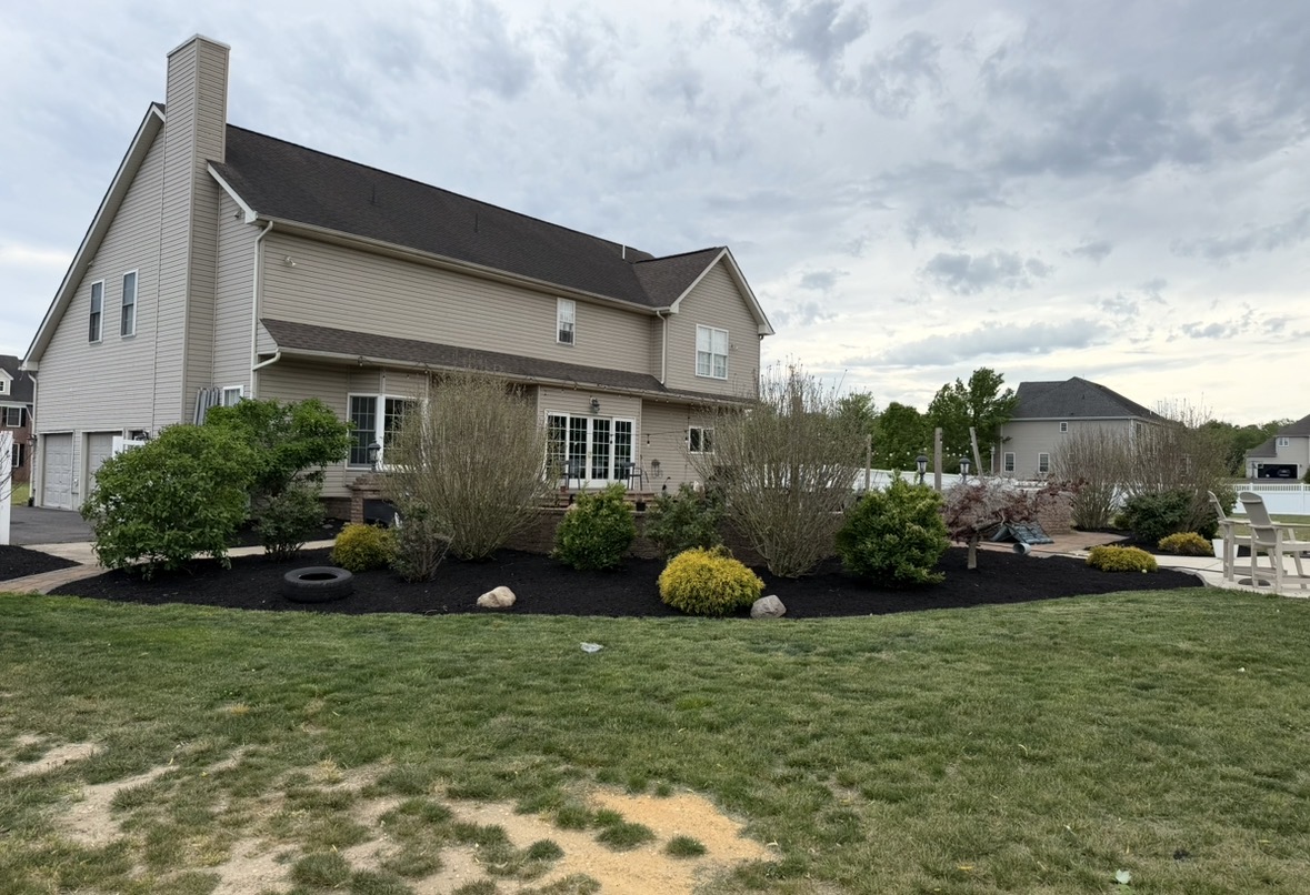 Wide curved mulch bed with shrubs and small trees wrapping the back of a two-story home
